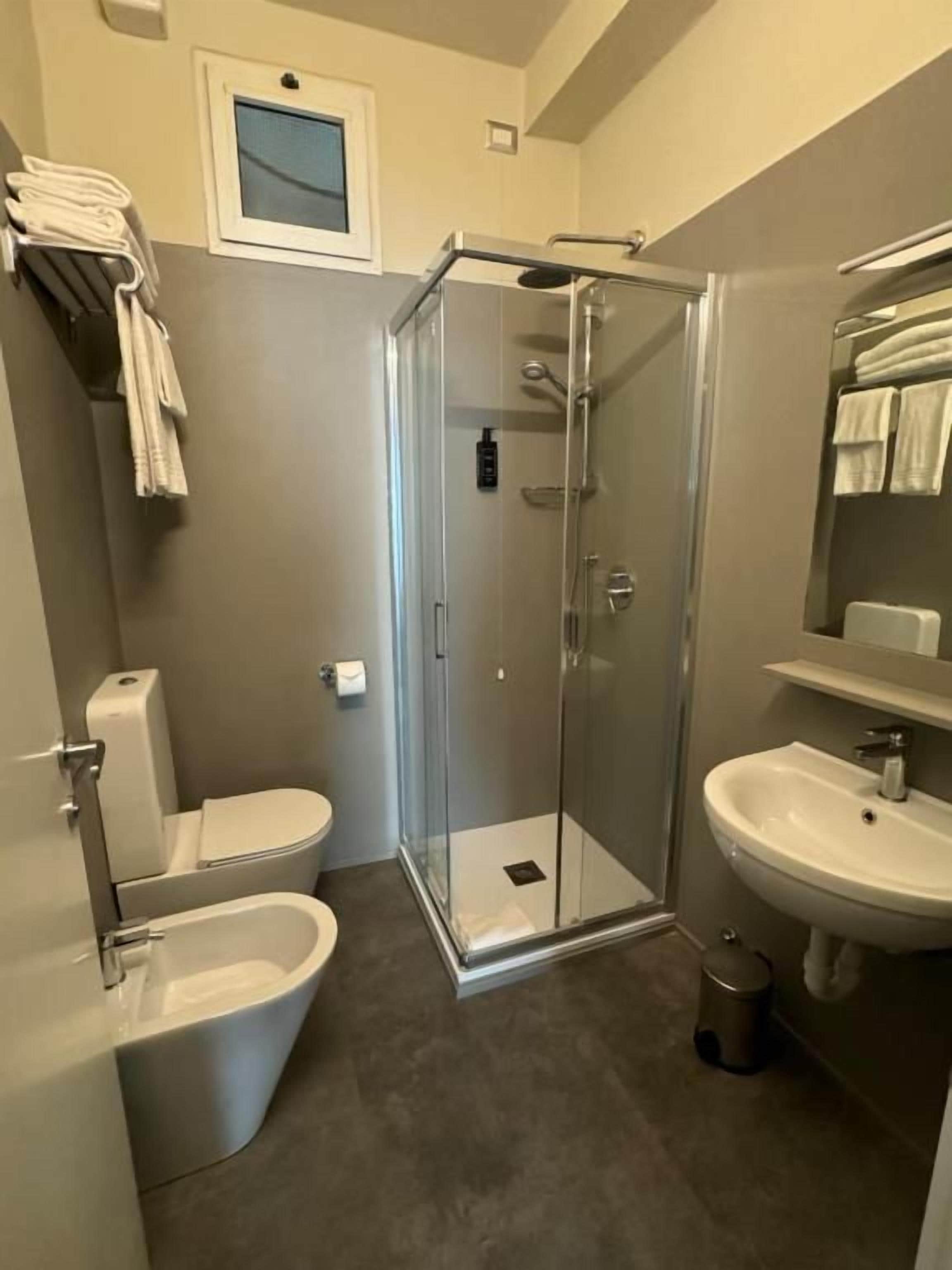 Een moderne badkamer met een douche met glazen wand, een toilet, een bidet en een wastafel.