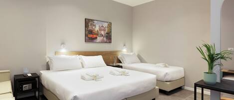 Habitación de hotel con dos camas, un cuadro en la pared, una mesita de noche con lámpara y una planta en maceta.