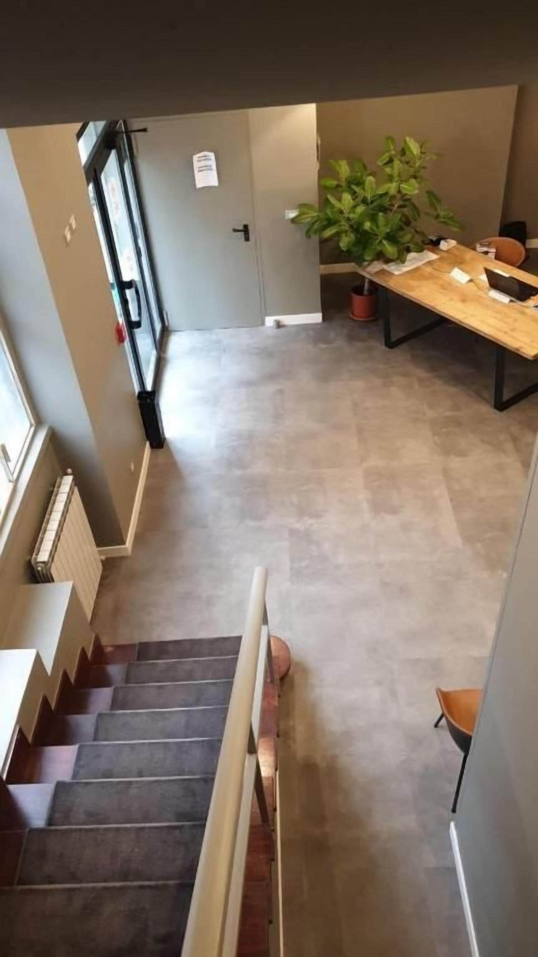 Una escalera conduce a una habitación con una mesa de comedor, una planta en maceta y una puerta con un letrero.