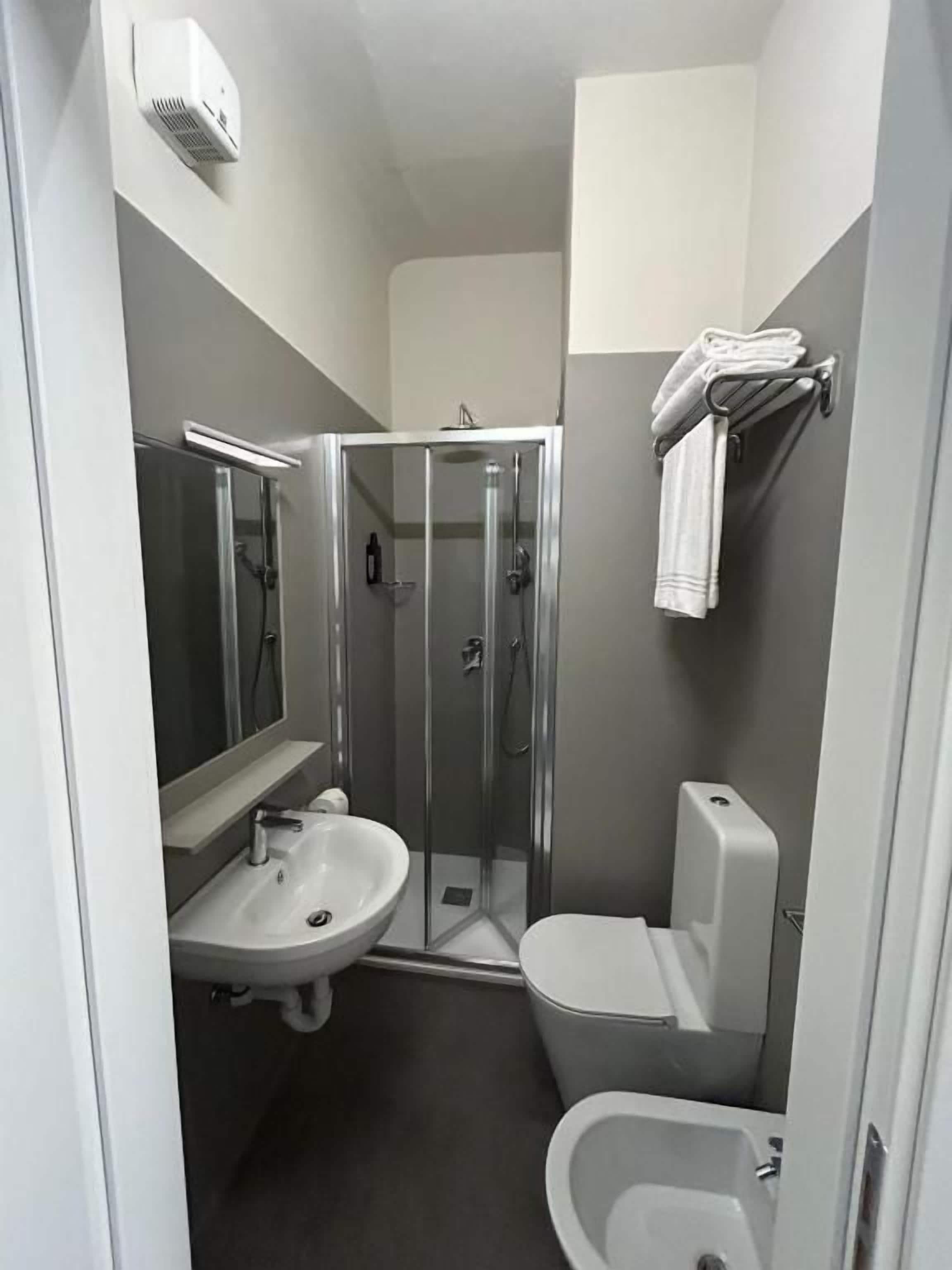 A compact bathroom with a glass-enclosed shower, a sink, and a toilet.