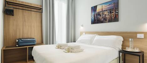 Habitación de hotel con una cama grande, cabecera de madera, un cuadro de un paisaje urbano, una mesita con un vaso y una maleta en un estante.