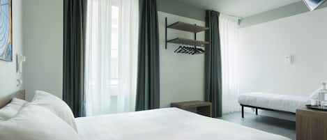 A hotel room with two beds, a wooden bedside table, a small bench, and a wall-mounted coat rack.