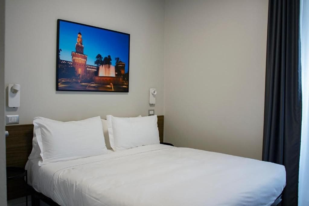A hotel room with a bed, white bedding, a wall-mounted picture of a tower, and a night sky.