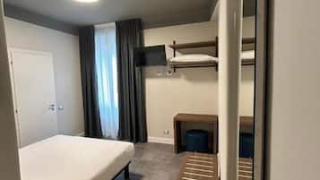 Ein kleines Hotelzimmer mit einem Einzelbett, einem kleinen Schreibtisch, einem Stuhl, einem Spiegel und einem Fenster mit Vorhängen.