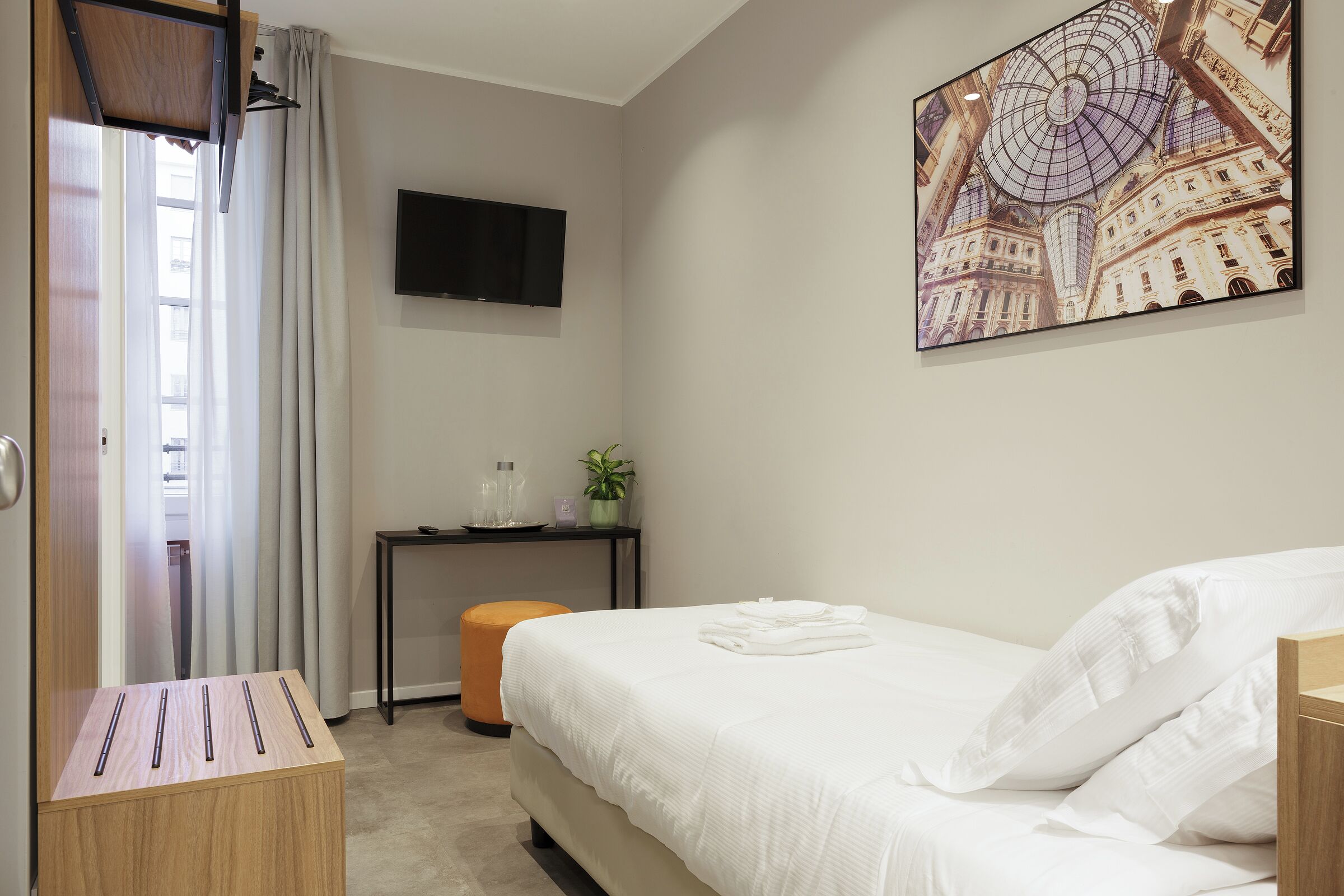 A hotel room with a bed, a desk, a television, and a painting on the wall.