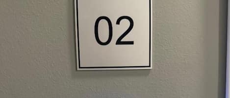 Una placa con el número '02' fijada a la pared y un panel de control con botones e indicadores iluminados.
