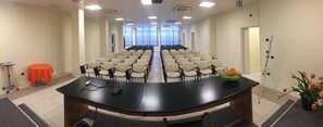 Ein Konferenzraum mit einem langen Tisch, Reihen von Stühlen, einem kleinen orangen Tisch und einer Blumenkomposition.