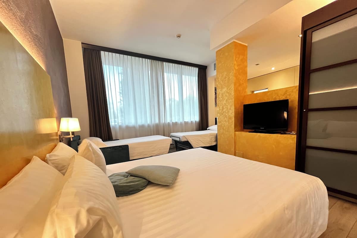 A hotel room with two beds, a TV, and a large window with curtains.