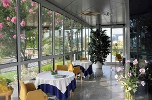 A restaurant with large windows, round tables, and chairs. - SMT EVOLUZIONE S.R.L. (San Paolo d'Argon)
