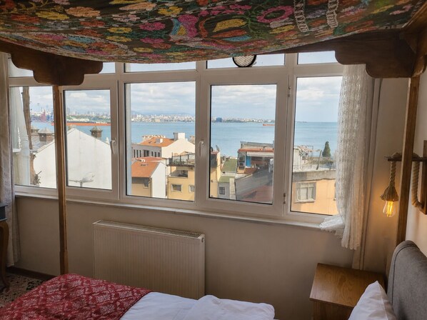 A bedroom with a large window, a bed, a radiator, and a view of a cityscape and water.
