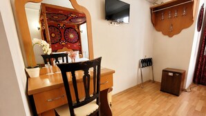 Een kamer met een houten bureau, een stoel, een televisie, een kledingkast en een airconditioner.
