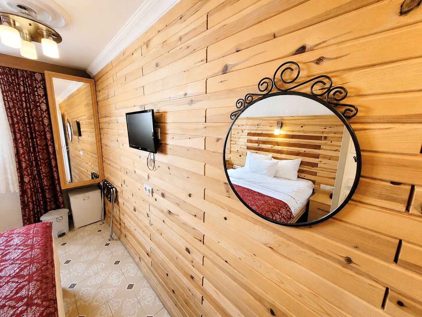 A wooden-paneled room with a bed, a TV, and a mirror.