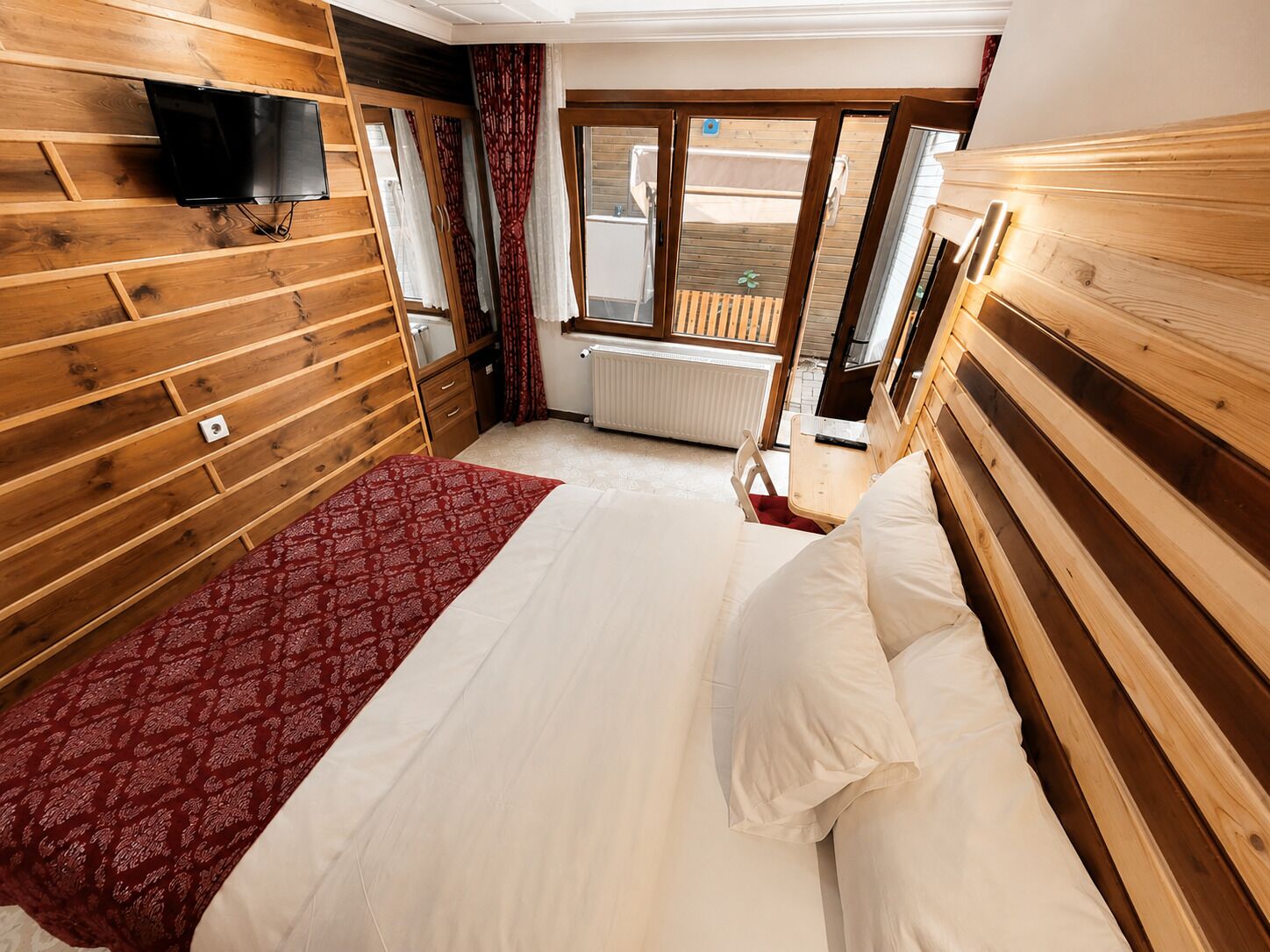 A wooden-paneled room with a bed, a TV mounted on the wall, and a window with a view.