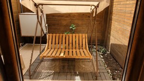 Een houten zitgedeelte buiten met een schommel, een plant en een rieten dak.