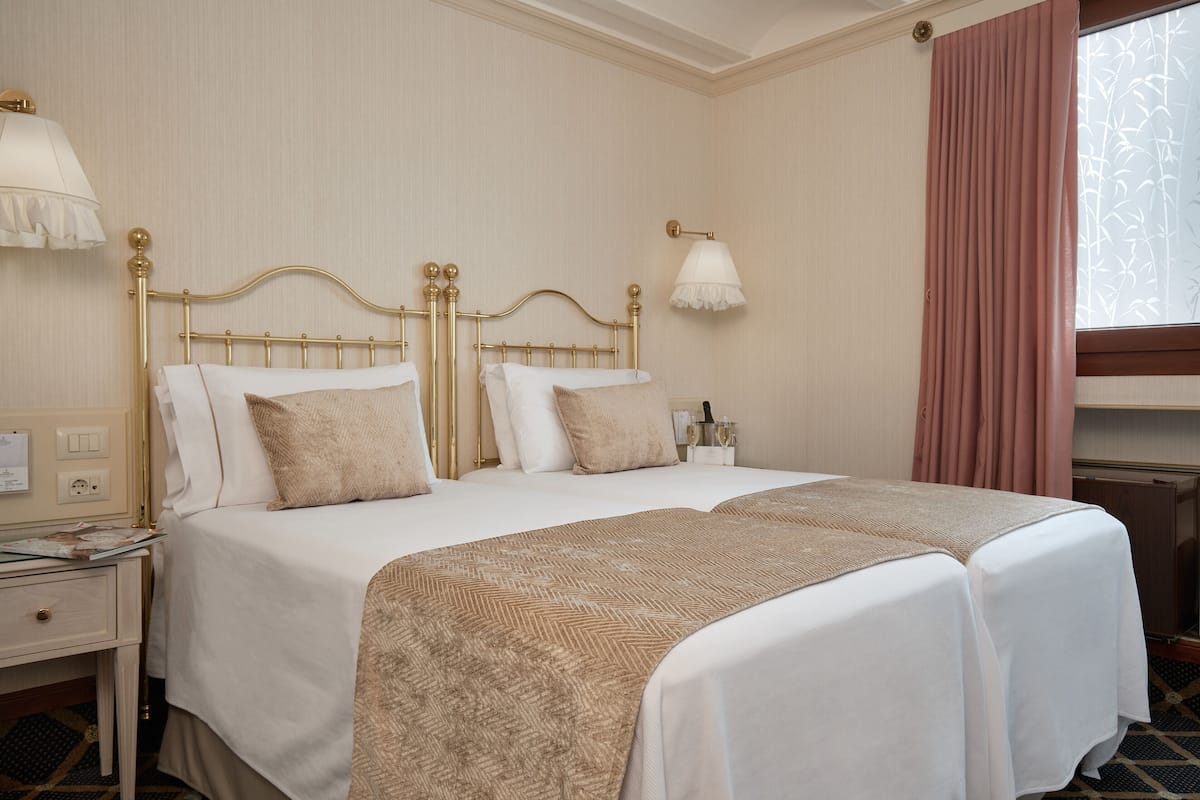 Un lit double avec un cadre doré, deux tables de chevet, une petite table, une lampe et une fenêtre avec des rideaux.