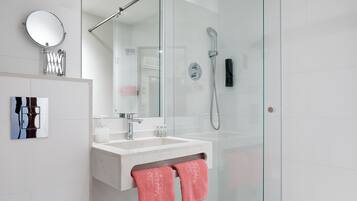 Un baño moderno con ducha envuelta en vidrio, un lavabo blanco y un espejo grande.