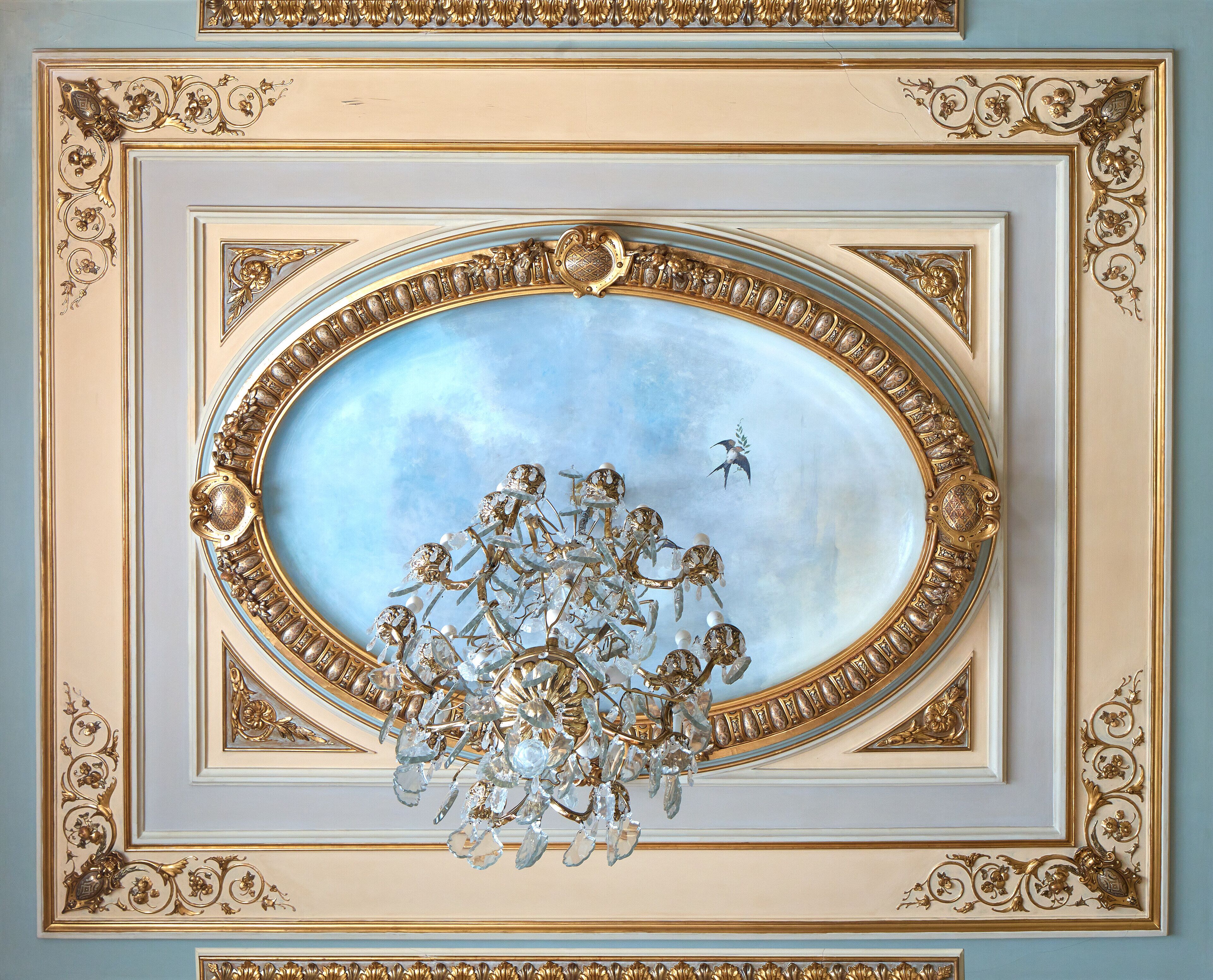 Techo con un tragaluz ovalado ornamentado que presenta un fresco de querubines y un pájaro volando.