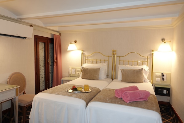 A hotel room with two beds, a desk, and a chair. There are lamps on either side of the beds and a tray with fruit and a drink on the bed. - Hotel Continental Palacete (Barcelona)