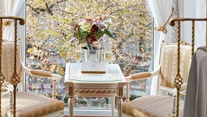 Una habitación de diseño clásico, con una mesa con un jarrón de flores, dos sillones tapizados y vistas a un árbol desde una ventana.