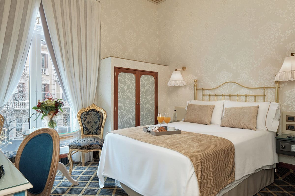 Une chambre d’hôtel avec un lit, une chaise, une table et une fenêtre avec des rideaux.