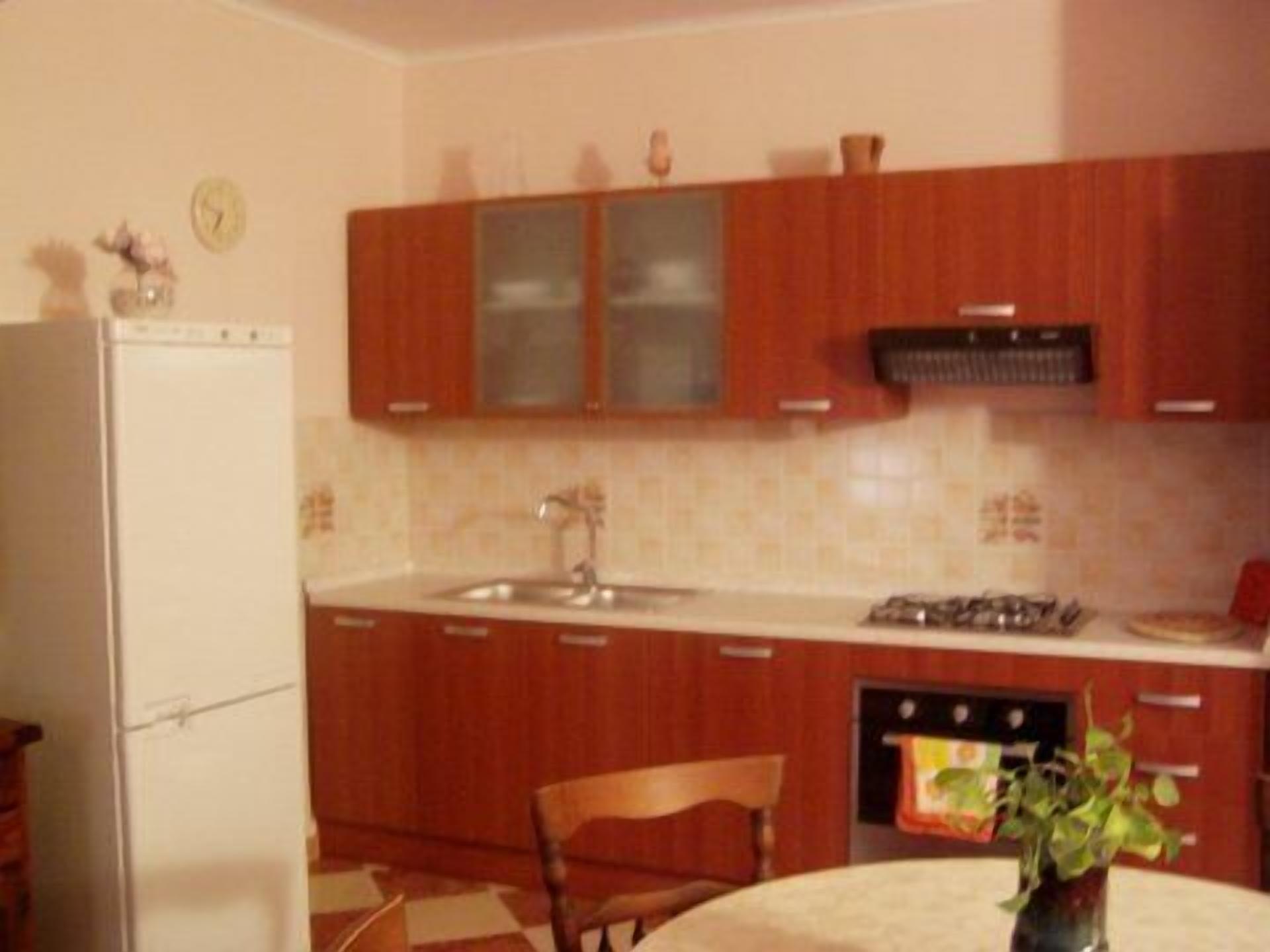 Une cuisine de taille réduite, avec des meubles en bois, un réfrigérateur blanc, un évier et une cuisinière.