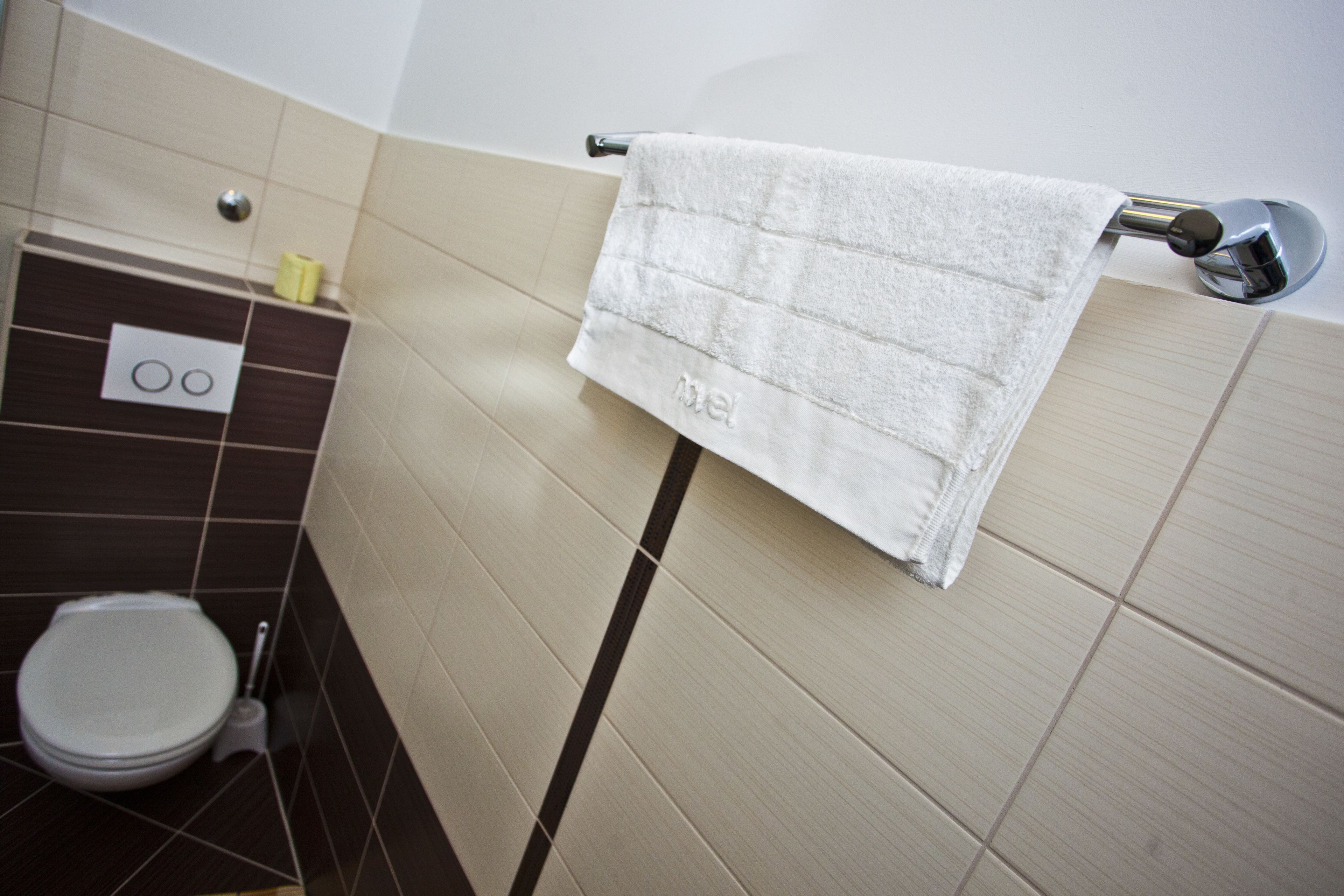 A bathroom with a toilet, a towel hanging on a rack, and a wall-mounted flush handle.