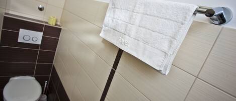 A bathroom with a toilet, a towel hanging on a rack, and a wall-mounted flush handle.