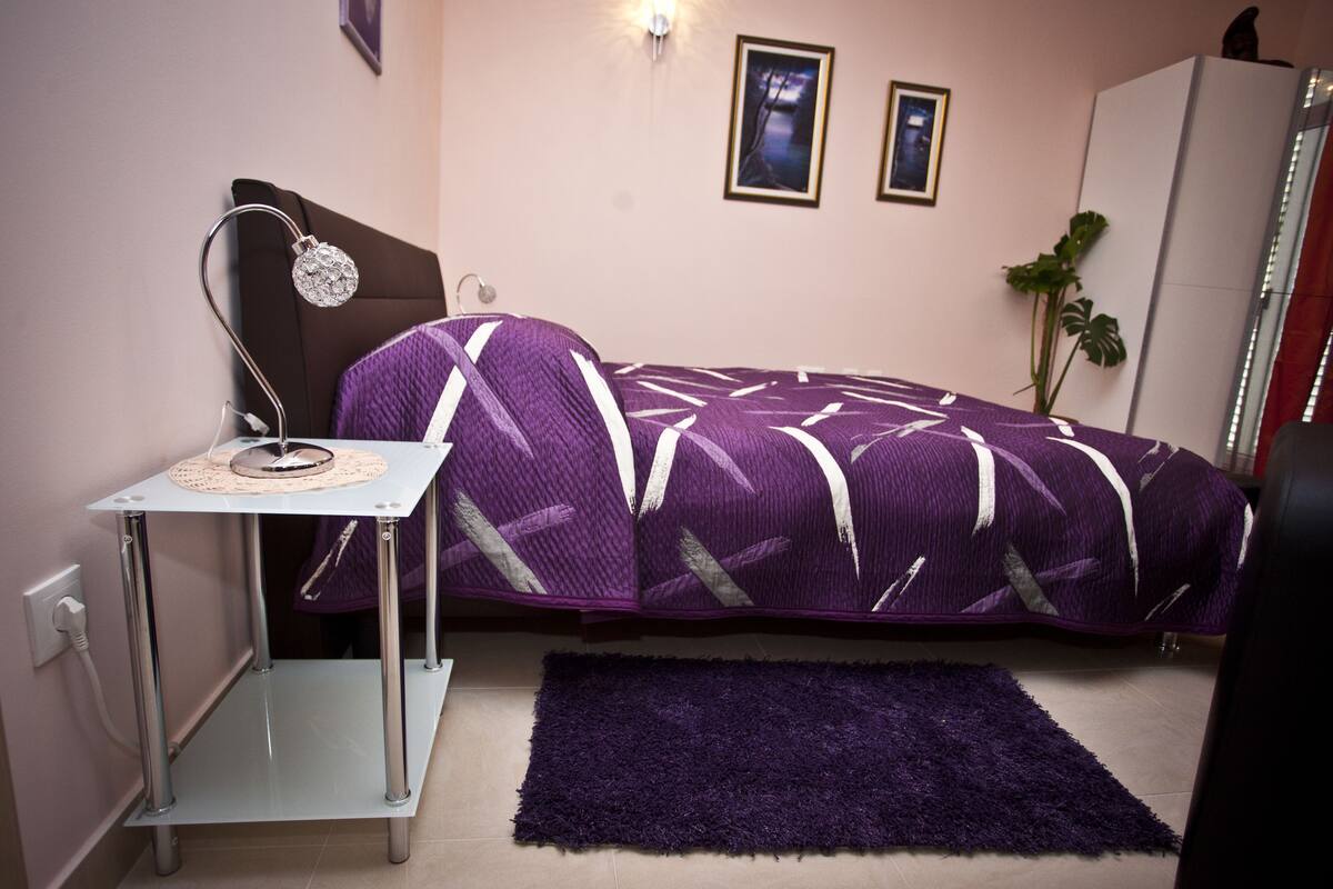 A bedroom with a bed, bedside table, lamp, and a small rug.