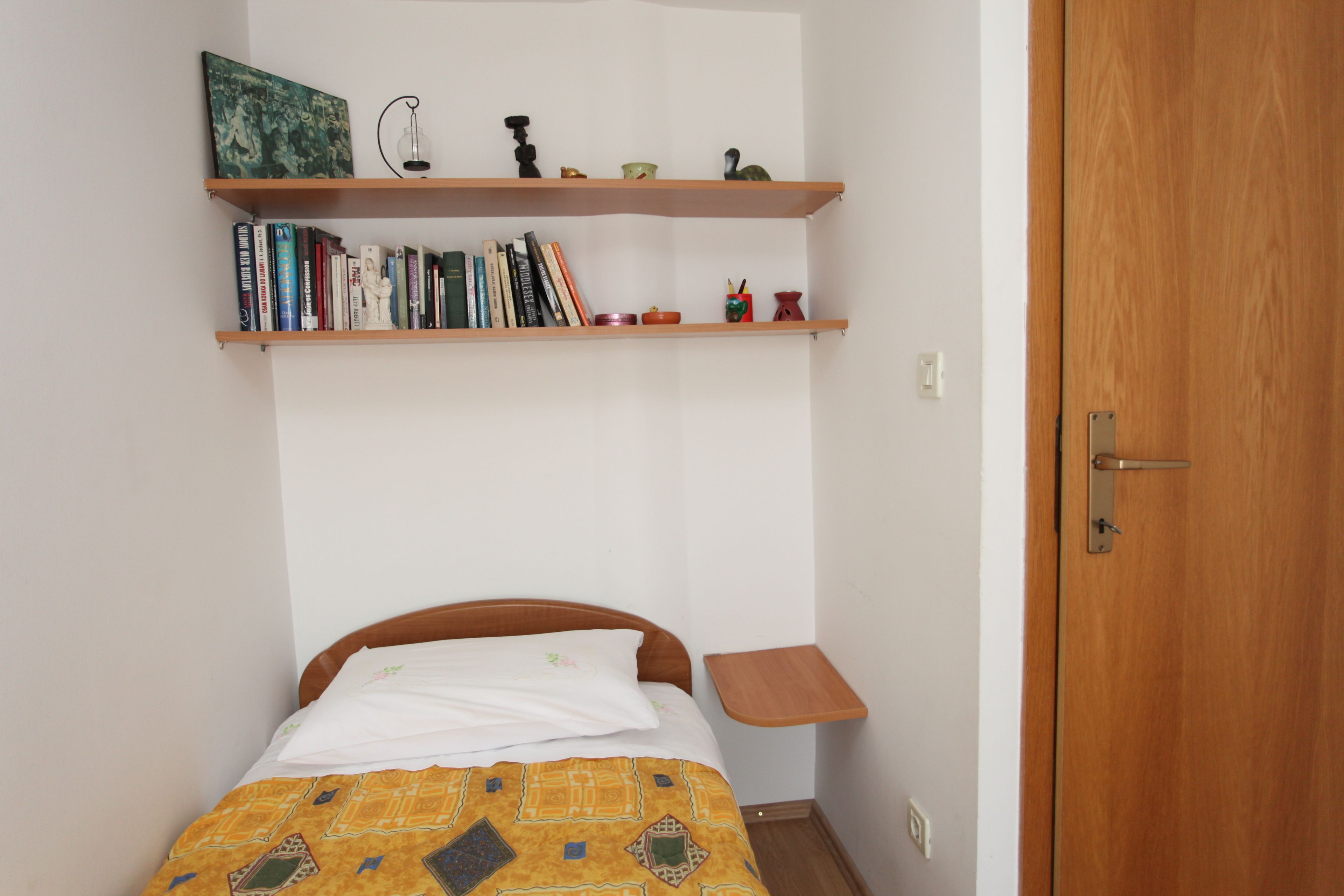 Un dormitorio con una cama, una mesita de noche de madera, una estantería y una puerta.