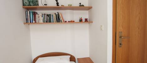 Un dormitorio con una cama, una mesita de noche de madera, una estantería y una puerta.
