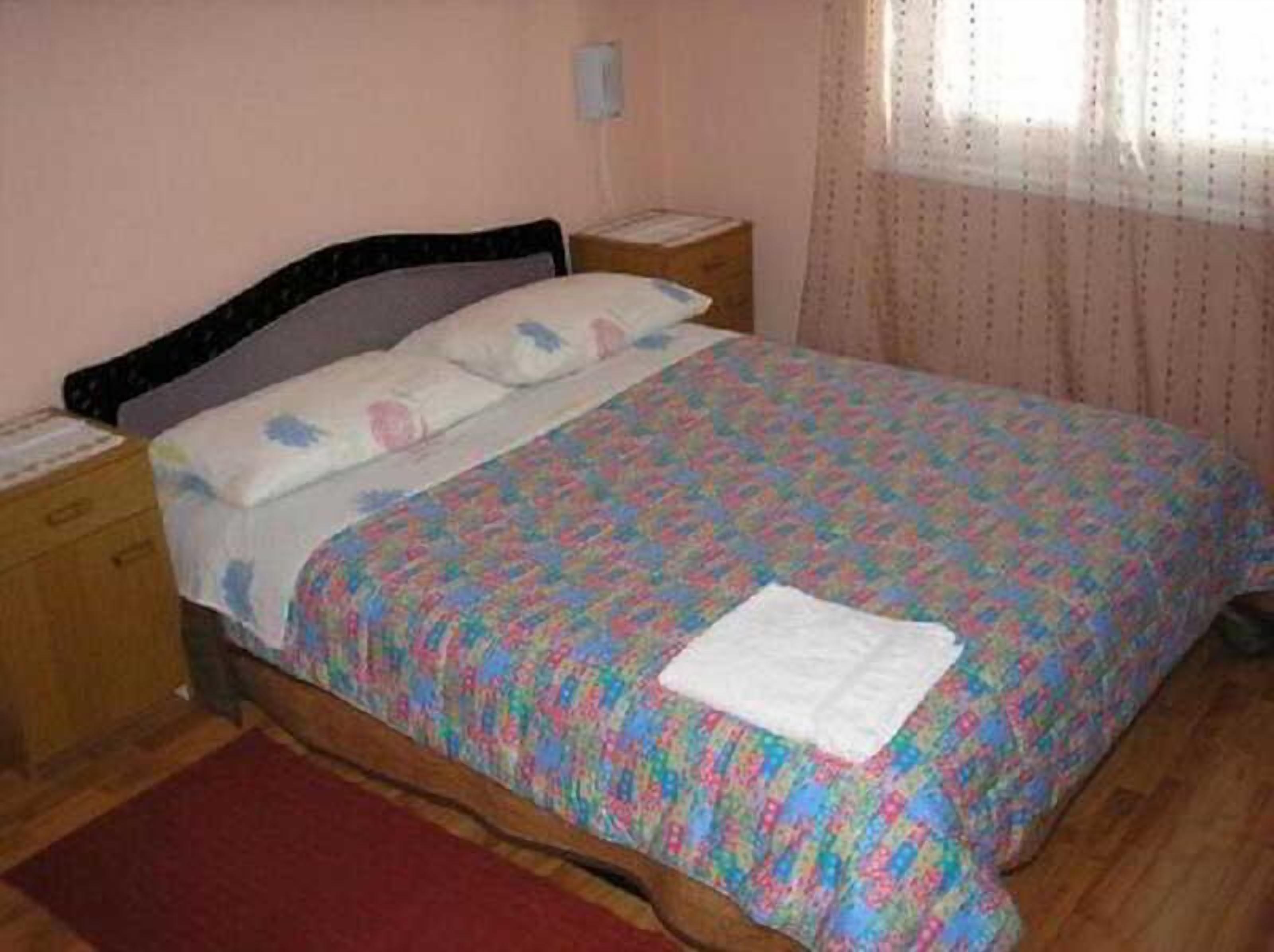 A single bed with a patterned bedspread, a nightstand, a bedside table, and a window with curtains.