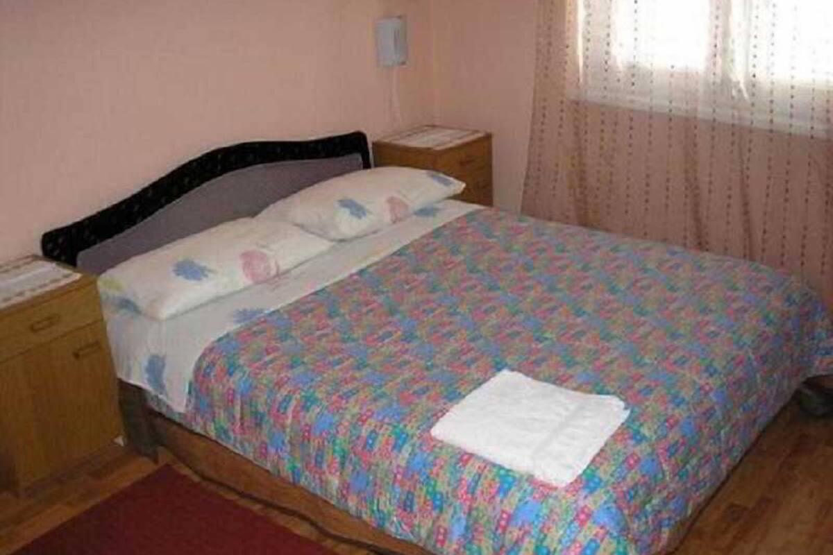 A single bed with a patterned bedspread, a nightstand, a bedside table, and a window with curtains.