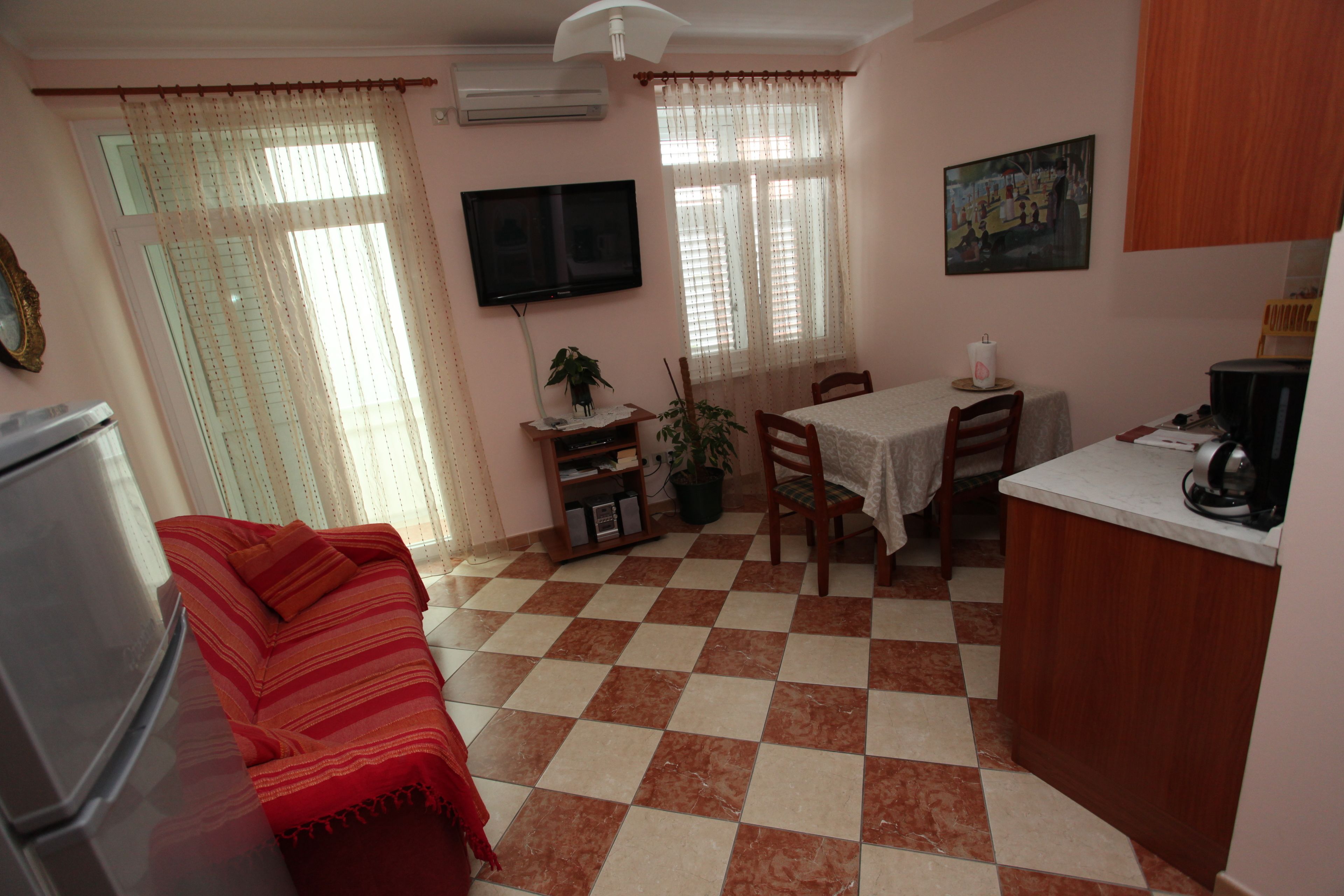 A compact living space with a kitchenette, a dining area, and a TV mounted on the wall.