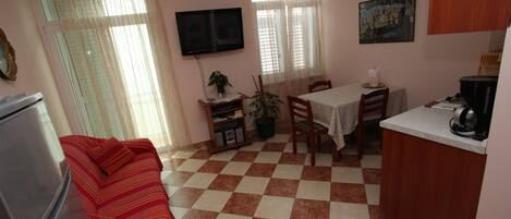 A compact living space with a kitchenette, a dining area, and a TV mounted on the wall.