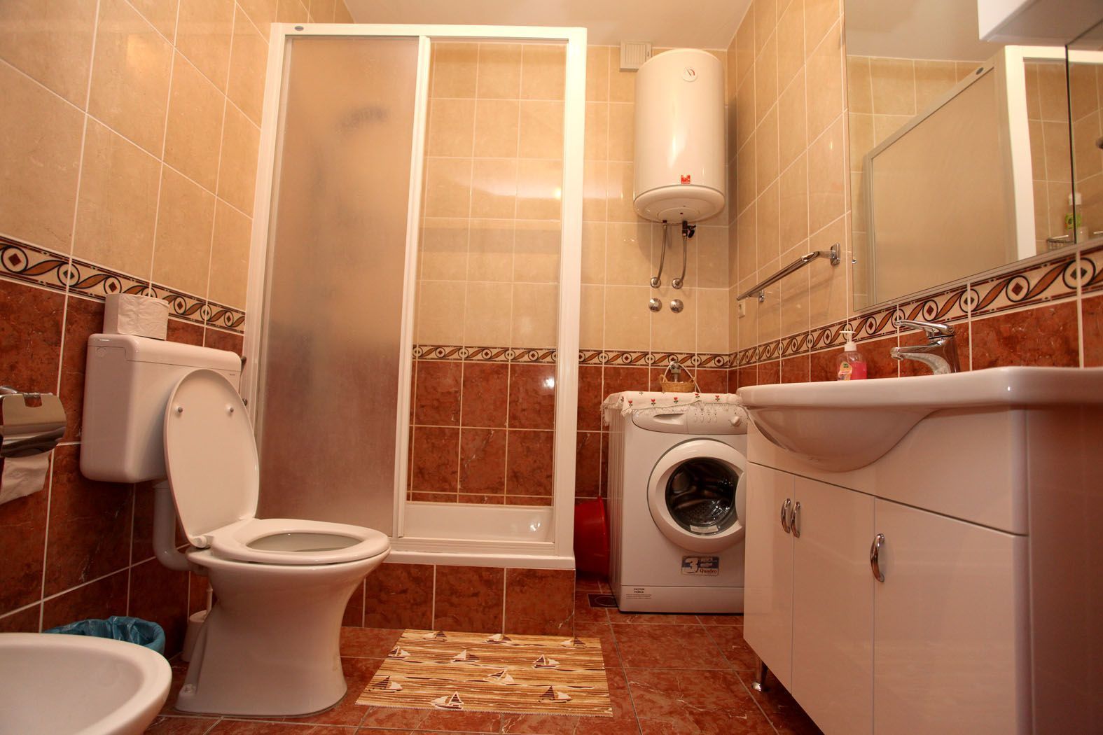 A bathroom with a toilet, shower, washing machine, and sink.
