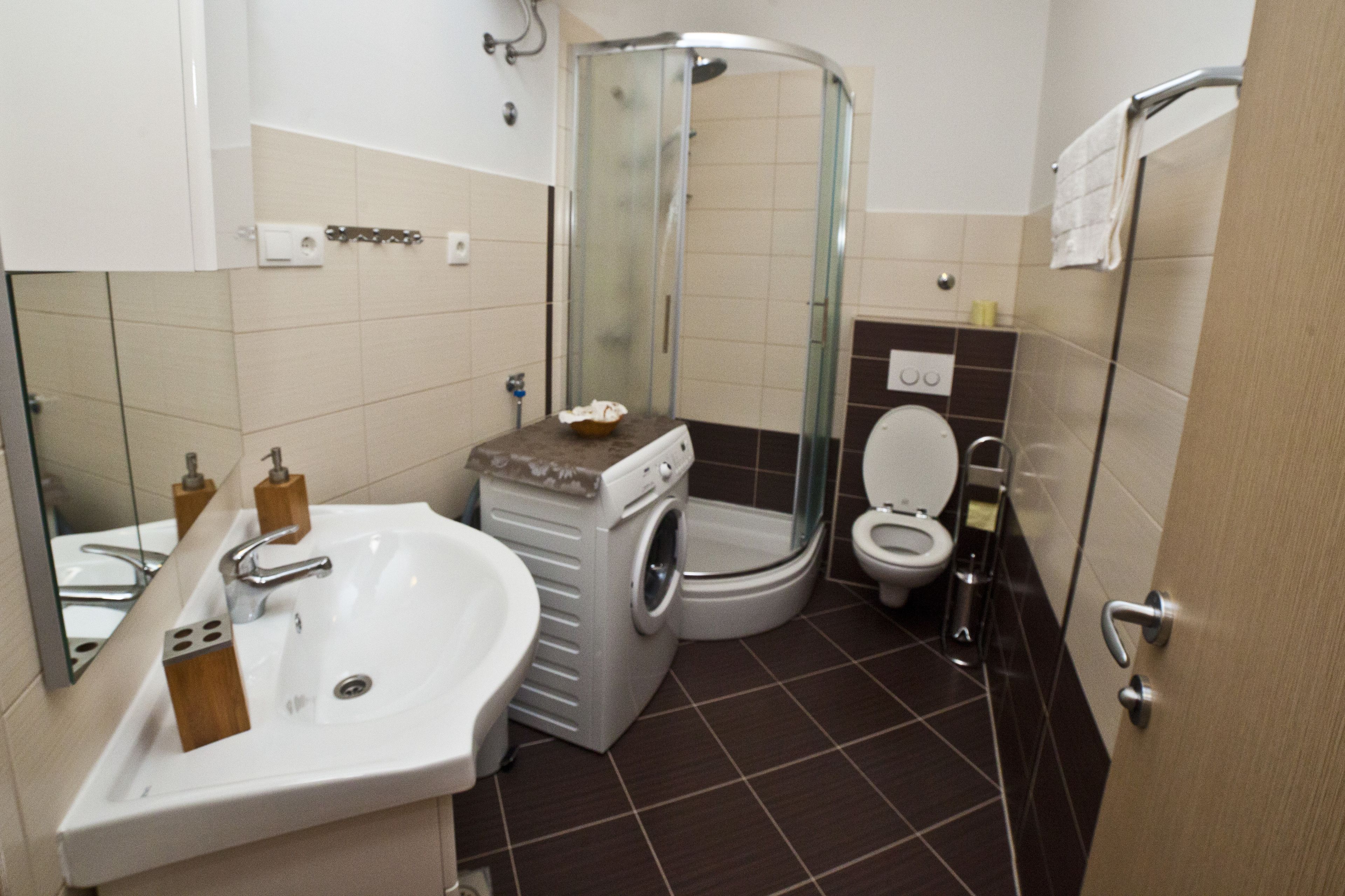 Et lille badeværelse med håndvask, toilet og en bruseniche med glasvægge.