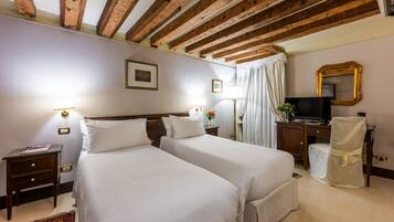 A hotel room with two beds, wooden beams on the ceiling, a television, and a desk with a chair.