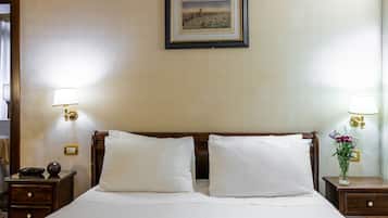 Une chambre d’hôtel avec un grand lit, deux tables de chevet, une commode, un tableau encadré au mur et un vase avec des fleurs sur la commode.