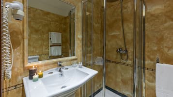 Un baño con lavamanos blanco, cabina de ducha con mampara de vidrio y un espejo.
