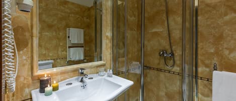 Un baño con lavamanos blanco, cabina de ducha con mampara de vidrio y un espejo.