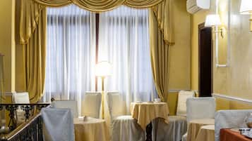 Une chambre d’hôtel dotée d’un coin repas comprenant quatre tables et chaises, une grande fenêtre avec des rideaux et une lampe.