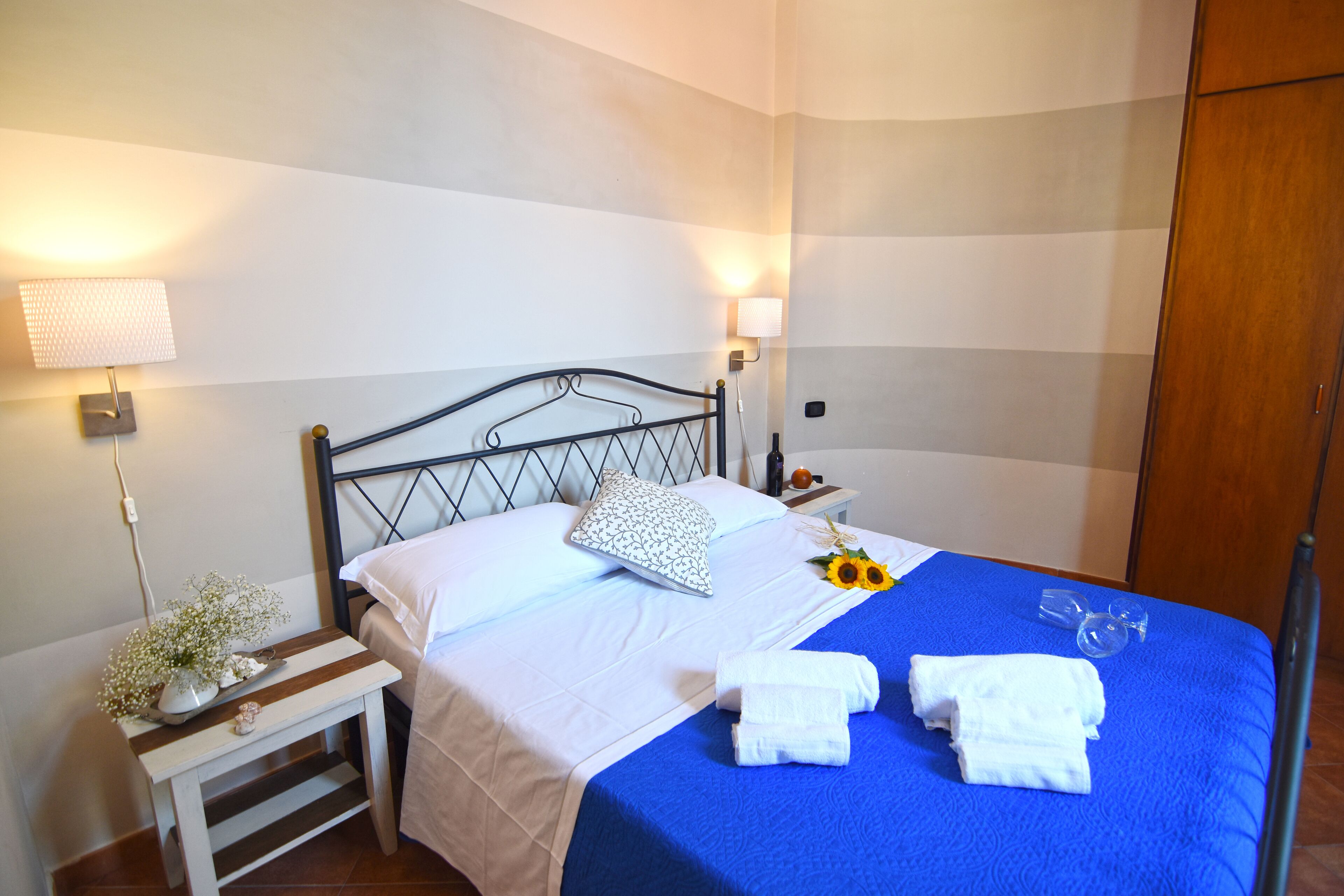 A neatly made bed with white and blue bedding, a bedside table with a lamp, and a wooden wardrobe.