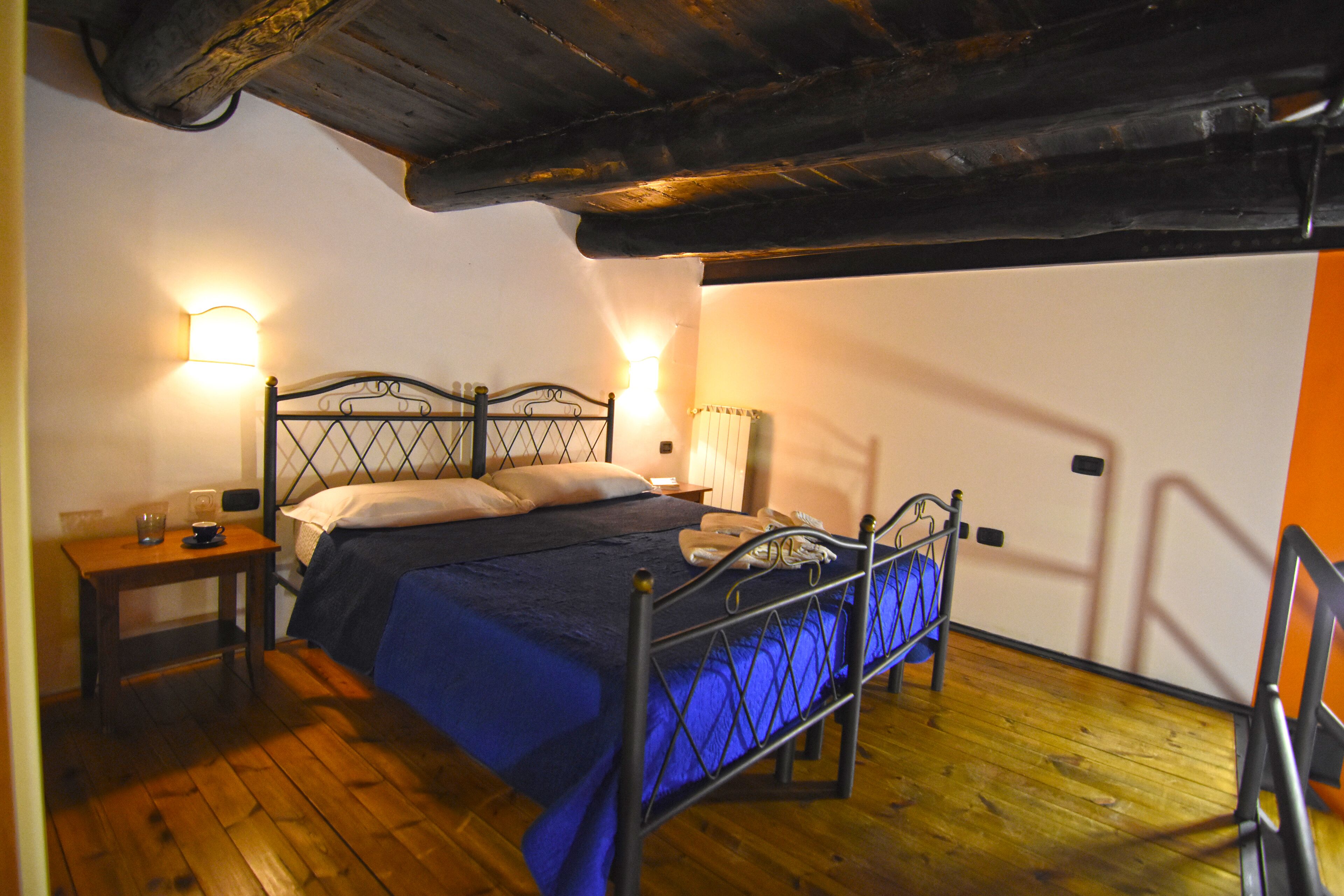 Une chambre avec un plancher en bois, un cadre de lit en métal, une table de chevet avec une lampe et un luminaire fixé au mur.