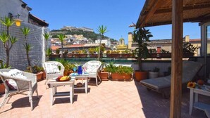 A rooftop terrace with wicker furniture, potted plants, and a view of a hilltop cityscape. - Case Così Chiaia (Naples)