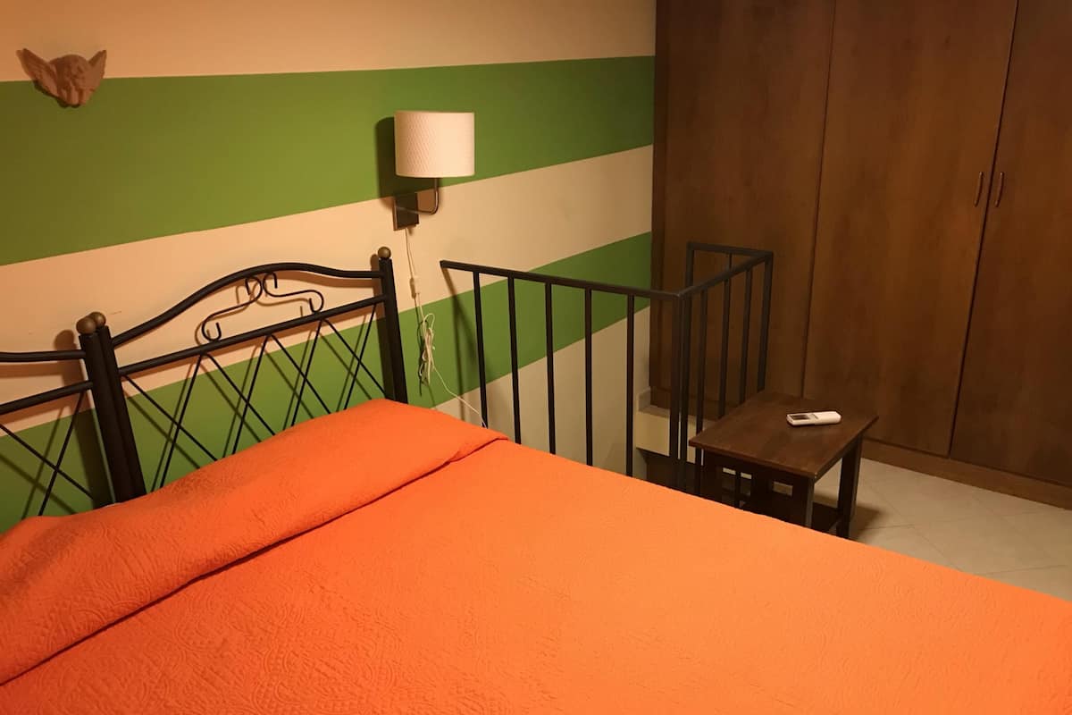 Une pièce comprenant un lit, une petite table, une lampe et un mur orné de rayures vertes et blanches.