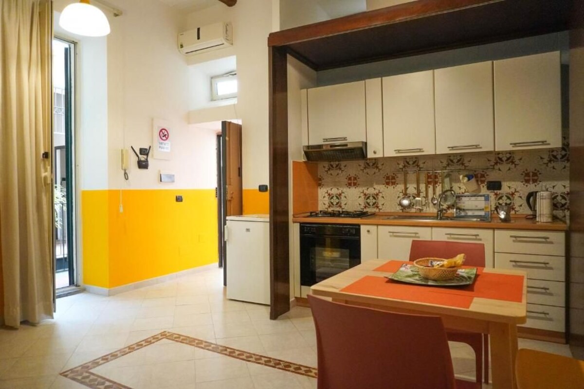 A compact kitchen with white cabinets, a small refrigerator, and a dining area with a table and chairs.