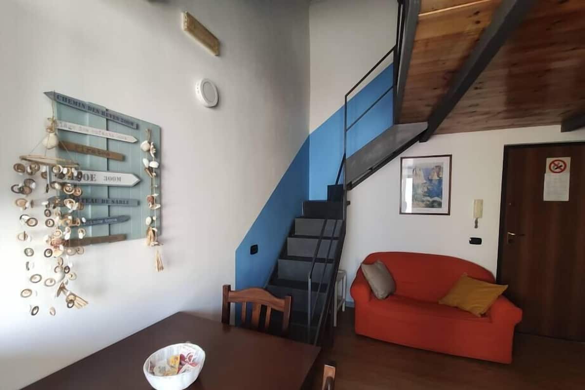 Un coin repas avec une table et des chaises en bois, un canapé rouge et un escalier agrémenté d’un mur d’accent bleu.
