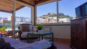 A balcony with a bed, a chair, a table, a potted plant, and a TV. - Case Così Chiaia (Naples)