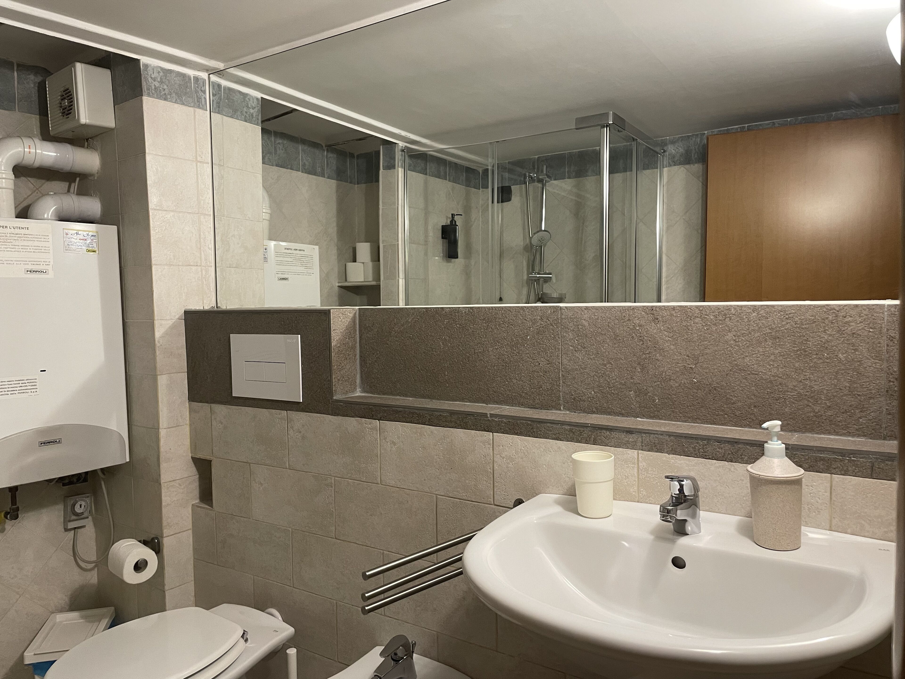 A bathroom with a toilet, sink, and shower. There are towels and a soap dispenser on the sink.
