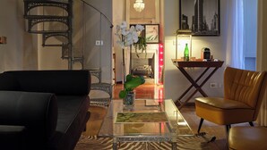 Un salon avec un escalier, une table basse en verre, un canapé, un fauteuil et un lustre.